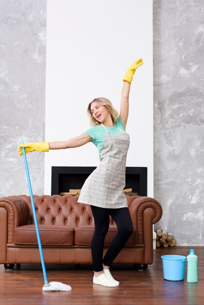 Nette Frau, die mit Reinigungsmopp nahe Couch aufwirft