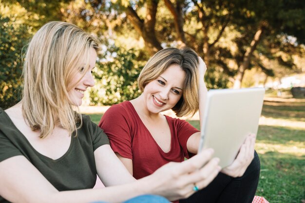 Nette Frauen, die Tablette im Park verwenden