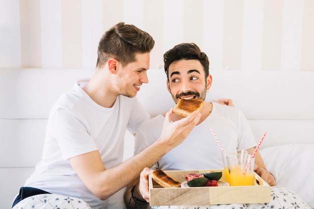 Nette homosexuelle Paare, die im Bett frühstücken