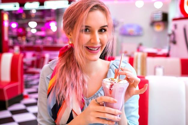 Nette hübsche sinnliche Frau mit trendigen rosa Haaren genießen ihren süßen Erdbeermilchshake, lächelndes, modisches Vintage-Pastell-Outfit