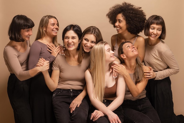 Nette interrassische junge und erwachsene Frauen in Freizeitkleidung, die sich auf beigem Hintergrund unterhalten