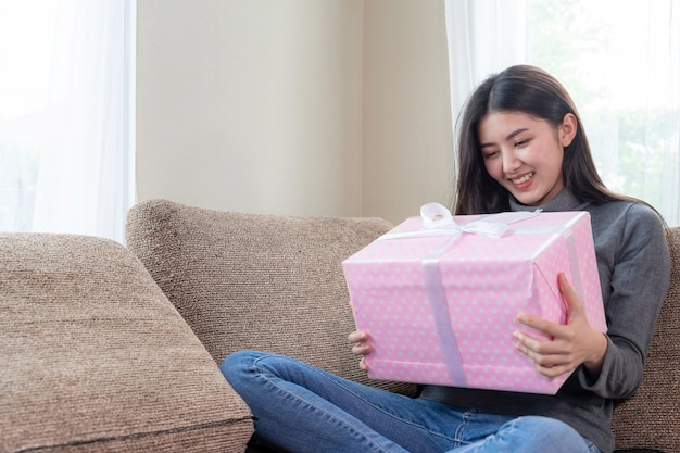 Nette Jugendfrau, die glücklich sich fühlt und die rosa Geschenkbox anwesend auf Couch umarmt