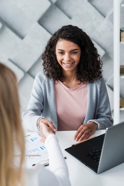 Kostenloses Foto nette junge brunettefrau, die hände mit dem kollegen sitzt im büro rüttelt