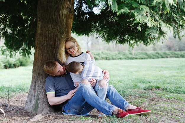 Nette junge Familie der Mutter, des Vatis und des kleinen Sohns haben Spaß, unter dem grünen Baum zu spielen