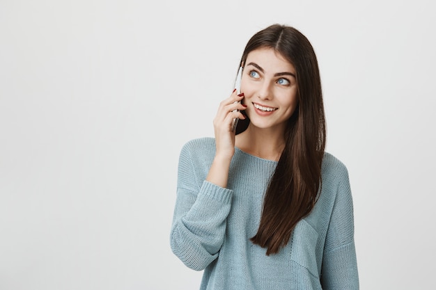 Nette junge Frau, die am Telefon spricht, lächelt und nach links schaut