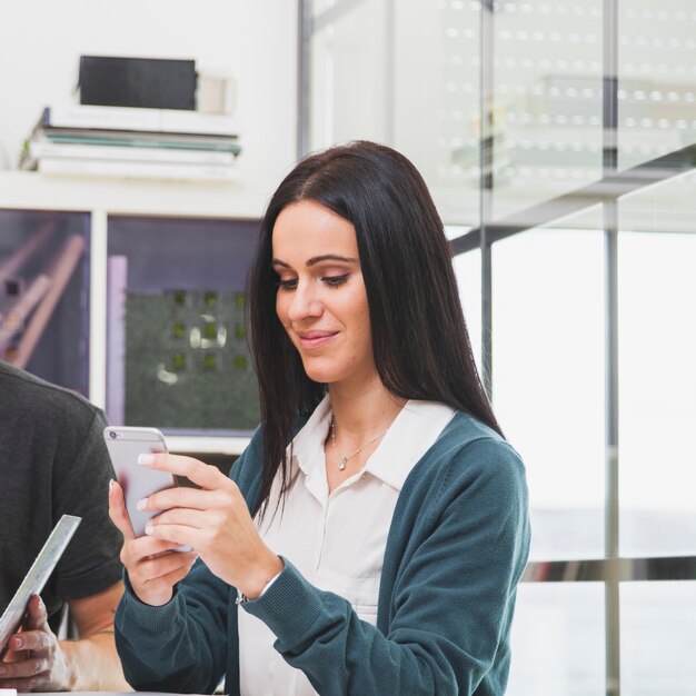 Nette junge Frau, die Telefon im Büro verwendet