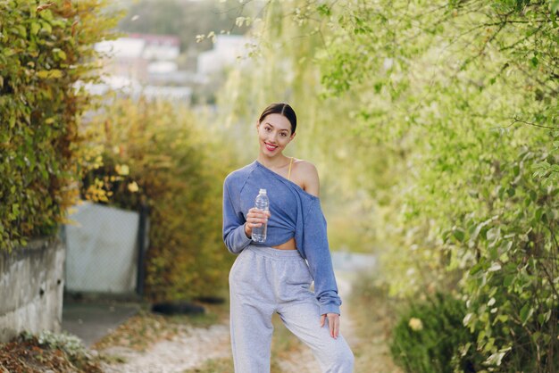 Nette junge Frau in Sportkleidung mit Flasche Wasser