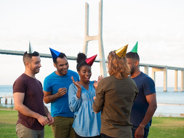 Nette junge Leute, die Geschenk für überraschtes Mädchen geben. Lächelnde Freunde, die junge Frau mit Geburtstag beglückwünschen. Konzept der Geburtstagsfeier