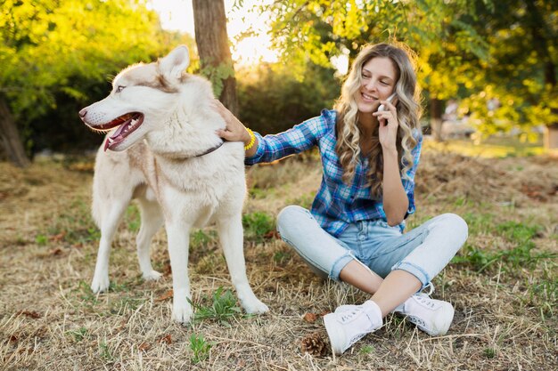 Nette junge stilvolle hübsche lächelnde glückliche blonde Frau, die mit Hund husky Rasse im Park am sonnigen Sommertag spielt