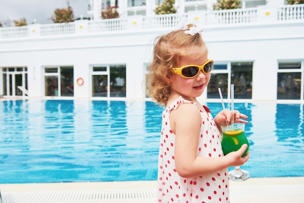 Nette kleine Blondine am Pool und hält einen Kindercocktail.