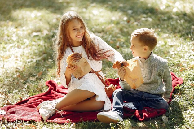 Nette kleine Kinder, die in einem Park mit Brot sitzen