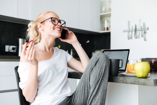 Nette lachende Dame bei der Unterhaltung auf Smartphone in der Küche