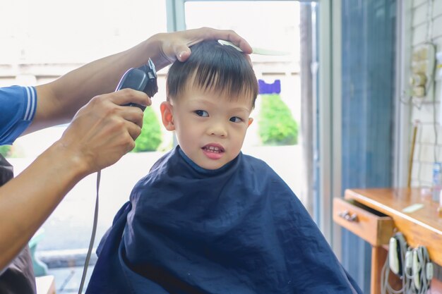 Kleiner Junge Der Haarschnitt Durch Friseur Beim Sitzen Im Stuhl Am Barbershop Erhalt Premium Foto