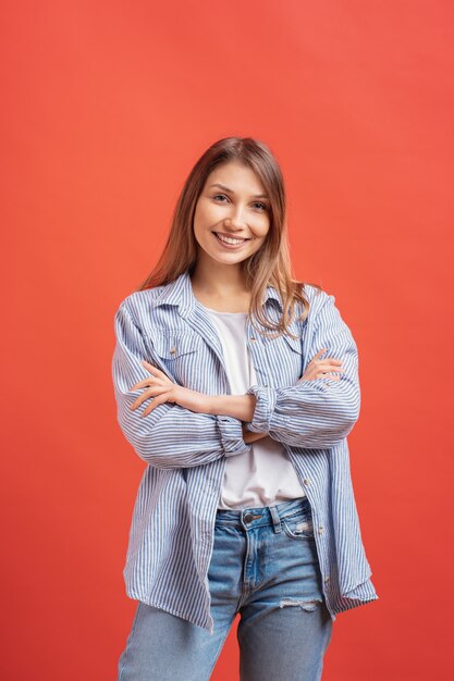 Nette langhaarige Frau, die mit verschränkten Armen aufwirft, lächelnder Gesichtsausdruck auf roter Wand.