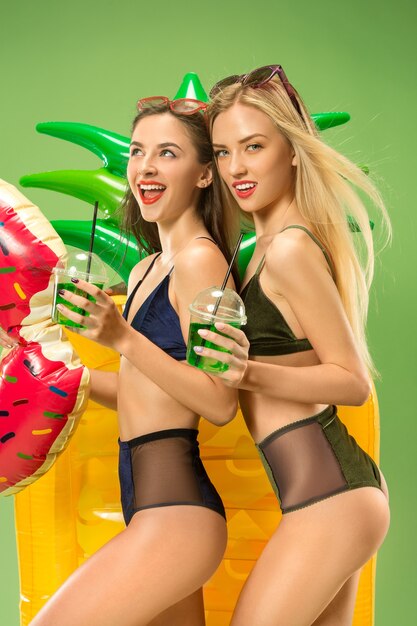 Nette Mädchen in Badeanzügen, die im Studio aufwerfen. Kaukasische Teenager des Sommerporträts auf grünem Hintergrund.