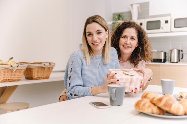 Nette Mutter und Tochter mit dem Geschenk, das Kamera betrachtet