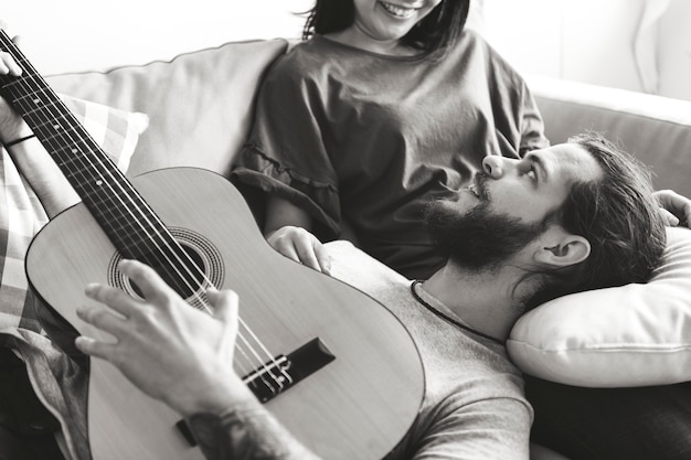 Nette Paare auf einem Couchfreund, der ein Gitarrenmusik- und -liebeskonzept spielt