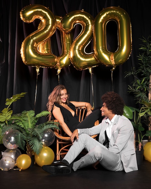 Nette Paare, die einander umgeben durch Ballone mit 2020 neuem Jahr betrachten