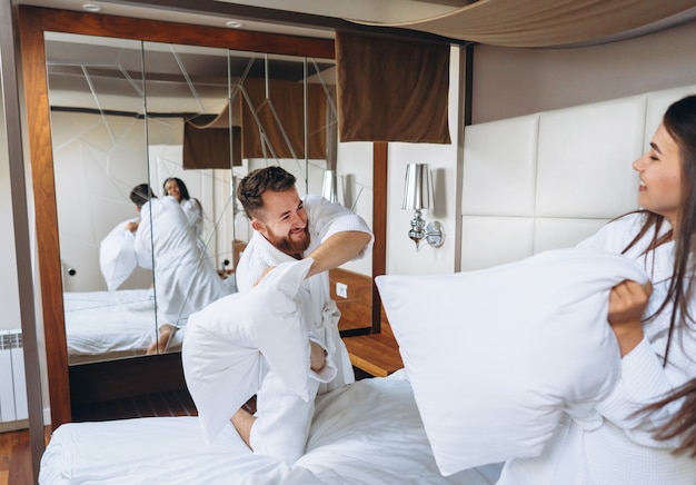 Nette Paare haben Spaß im Schlafzimmer, das zu Hause mit großen Kissen kämpft