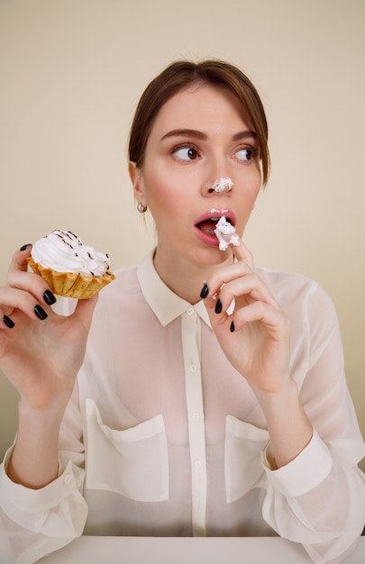 Nette reizende junge Frau, die sitzt und Kuchen durch Finger isst