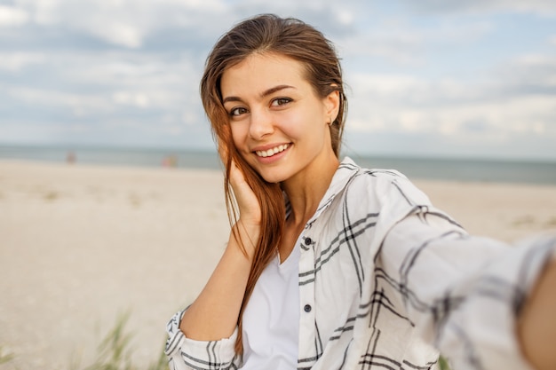 Nette romantische frau, die auf sonnigem strand, windigen haaren, ausdruck, sommerstimmung aufwirft. selbstporträt.