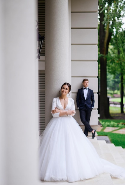 Nette schöne junge Brautfrau im geschwollenen eleganten weißen Kleid, das draußen mit Bräutigam auf Hintergrund aufwirft Hochzeitstag photosession Sommerzeremonie Brides Marriage