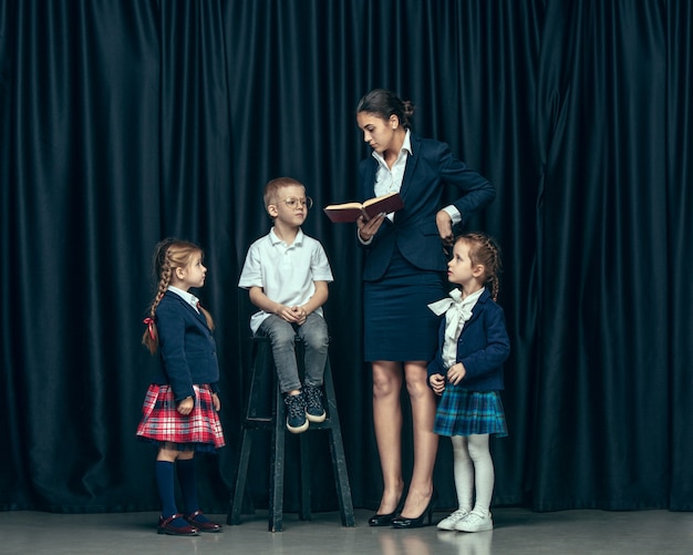 Nette stilvolle Kinder auf dunklem Studio. Die schönen jugendlich Mädchen und Jungen, die zusammen stehen