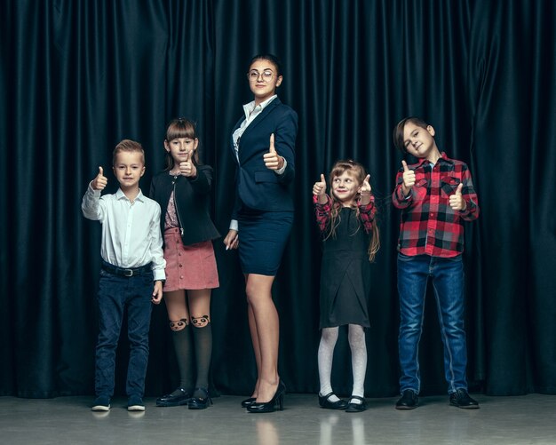 Nette stilvolle Kinder auf dunklem Studiohintergrund. Die schönen jugendlich Mädchen und Jungen, die zusammen stehen