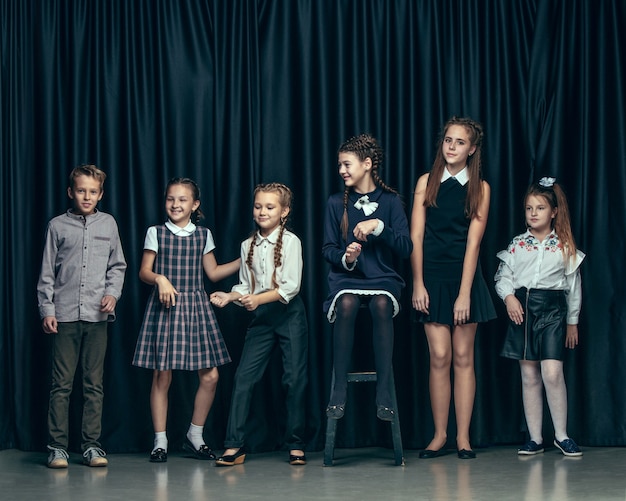 Nette stilvolle Kinder auf dunklem Studiohintergrund. Die schönen jugendlich Mädchen und Jungen, die zusammen stehen