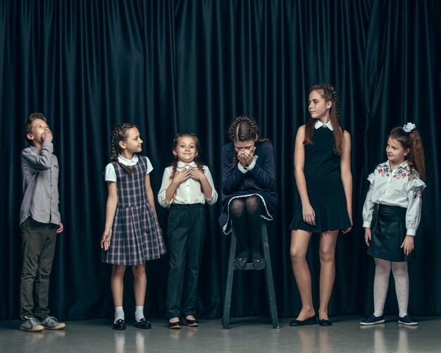 Nette stilvolle Kinder auf dunkler Studiowand. Die schönen jugendlich Mädchen und ein Junge, die zusammen stehen