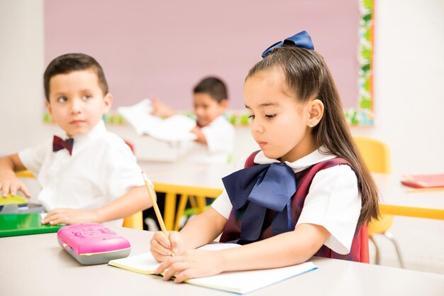 Nette Vorschulkinder, die eine Uniform tragen und eine Schreibaufgabe in einem Klassenzimmer erledigen