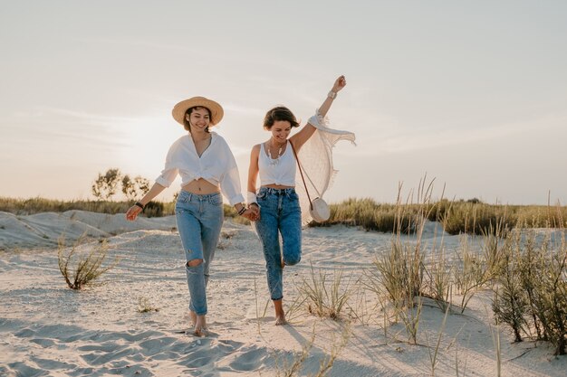 Nette zwei junge Frauen, die Spaß am Sonnenuntergangsstrand haben, schwule lesbische Liebesromantik