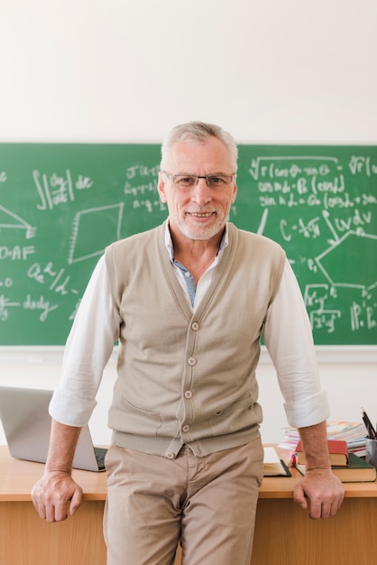 Kostenloses Foto netter älterer professor, der nahen lehrerschreibtisch im hörsaal steht