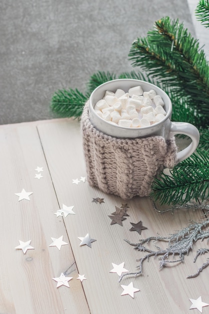 Netter Becher voller Marshmallows, umgeben von Weihnachtsschmuck auf dem Tisch