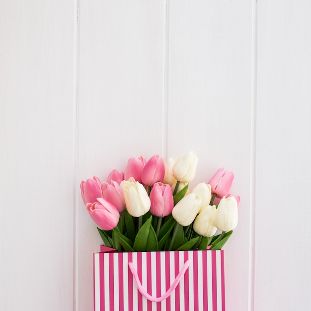 Netter Blumenstrauß von Tulpen innerhalb einer weißen und rosa Tasche auf einem weißen hölzernen Hintergrund