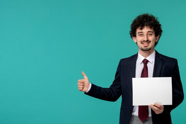 Netter hübscher Kerl des Geschäftsmannes im schwarzen Bürooutfit, das gutes Gestenzeichen zeigt und Papier hält