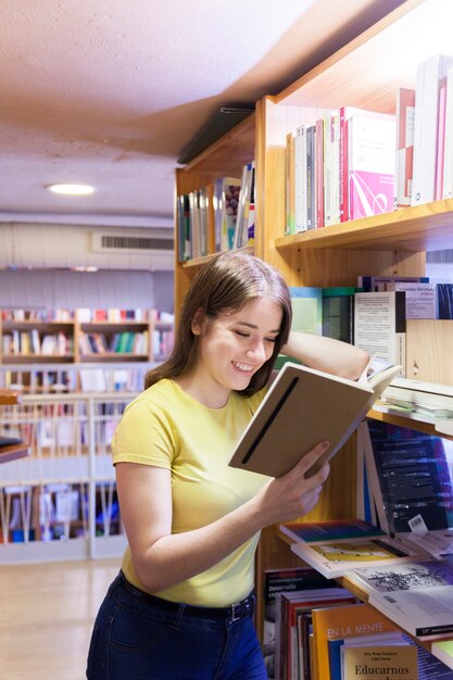 Netter Jugendlicher, der auf Bücherschrank und dem Lesen sich lehnt