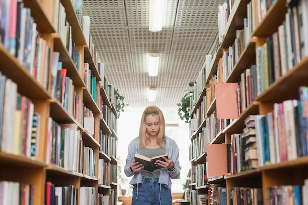 Netter Jugendlicher, der zwischen Bücherregalen liest