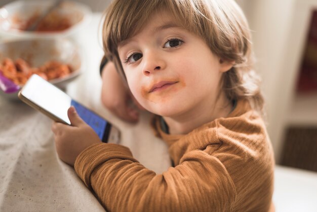 Netter Junge, der bei Tisch Telefon hält