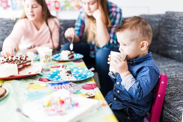 Netter Junge, der Kuchen trinkt und isst