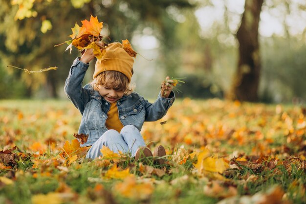 Netter Junge, der mit Blättern im Herbstpark spielt