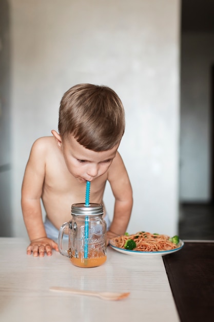 Netter junge, der teigwaren isst und saft trinkt