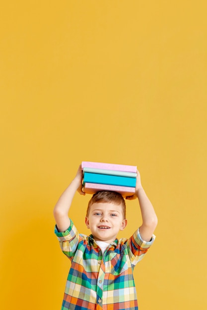 Netter Junge des Kopierraums mit Büchern auf seinem Kopf