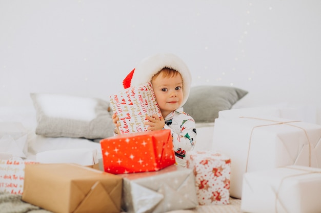 Netter Junge in der Weihnachtsmütze, die Geschenke an Weihnachten öffnet