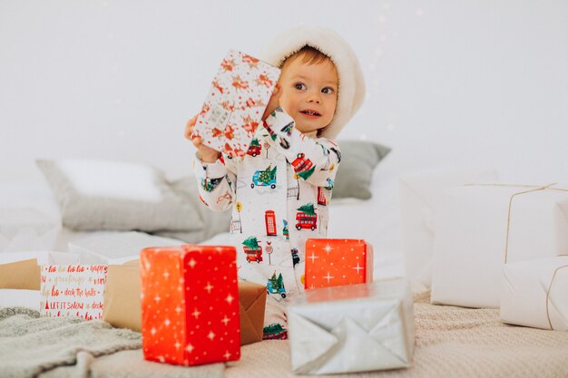 Netter Junge in der Weihnachtsmütze, die Geschenke an Weihnachten öffnet