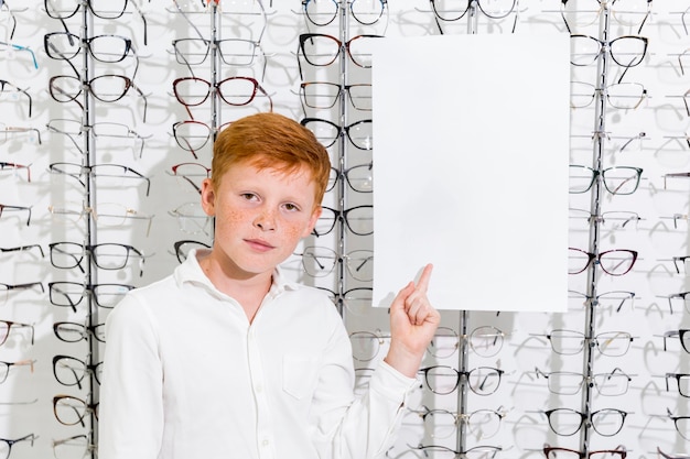 Netter Junge mit Sommersprosse auf Gesicht zeigend auf schwarzes Weißbuch im Optikshop