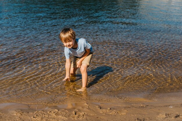 Netter Junge rührendes Wasser am Strand