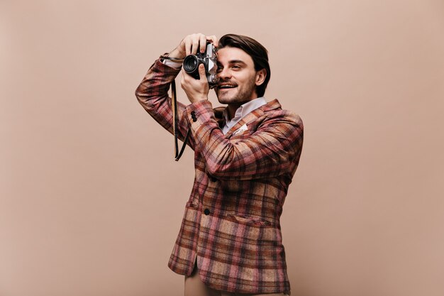 Netter junger Fotograf mit brünetten Haaren, in trendiger karierter Jacke, die Foto macht und lächelt