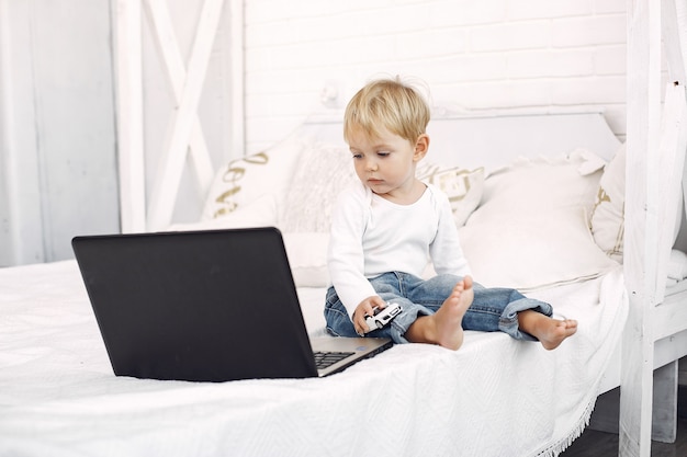 Netter kleiner junge, der mit einem laptop auf einem bett spielt