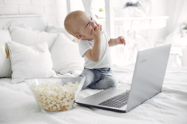 Netter kleiner Junge, der mit einem Laptop auf einem Bett spielt